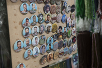 A square wooden board displays a range of martyrdom-­related pinup buttons for sale at a market in Tehran, Iran. Although all badges are of the same size and circular shape, they differ in color and what they depict. Most display a picture of a martyr with a Farsi caption, but some feature writing only and others depict an individual only.