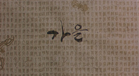 A large black calligraphic character can be seen behind a dense foreground of vertical smaller brown characters and some decorative pieces.