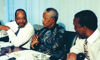 Zuma, President Mandela, and Tambo Mbeki having a discussion while seated at a table.