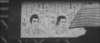 A man stands before several wanted posters, which have head and shoulder drawings of criminals, surrounded by explanations in calligraphy.