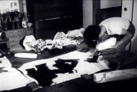 A man bows painting large black calligraphy on paper, in black and white cinematography.