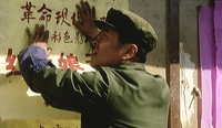 A man posts a poster to a wall with red calligraphy.