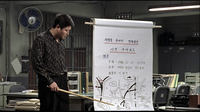 A man uses a ruler to point to a street map with black and blue calligraphy written on it.