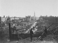 A black and white photograph of a destroyed city (Strasbourg), with two soldiers in the foreground standing in ruins. Several buildings remain standing in the distance.