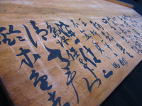 Detail photograph of a wooden board with black calligraphy.