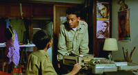 A shot from A Brighter Summer Day showing two junior high students in a room with a recorder on the desk and four Elvis Presley posters on the wall.