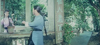 A romantic scene between two characters. The frame is bisected by a large pillar with a sign with green characters painted onto it, a love poem.
