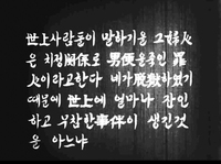 An underlit wooden surface has white calligraphy superimposed over it, in black and white cinematography.