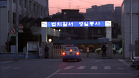 A gateway entrance has a lit sign with white calligraphy printed on it.