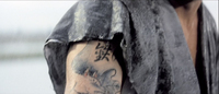 Calligraphy is visible on a tattooed arm, partially covered by a sleeve.