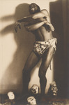 Publicity photo of Habib Benglia dancing at the Folies Bergère, Paris, in 1921. He is shirtless and smiling while posing. There are four African masks on the floor.