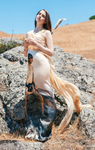 A model stands in a rocky landscape wearing a peach, silk evening gown. The dress is printed with an image of Luke Skywalker. The train on the dress flows in the breeze.