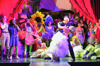 Performers Taylor Mac and Davina Cohen dressed as a bride and groom, surrounded by actors dressed as flowers.