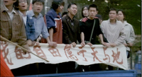 A row of men hold onto a railing draped by a sign, with red calligraphy.