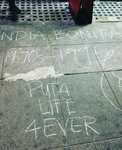 Chalk writing on a sidewalk reads “India Bonita 1970s–1996 Puta Life 4Ever.”