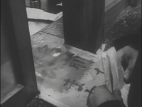 The floor in an entranceway has black calligraphy drawn on it, in black and white cinematography.