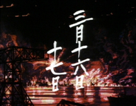 White calligraphy of the date of an American bombing is superimposed over a series of explosions and flames in a residential district.