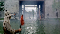 A man stands guard at a water gateway with white subtitle calligraphy superimposed over it.