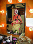 Performer Taylor Mac wearing a dress made of latex gloves and looking in a makeup mirror.