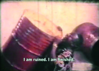 Film still frame of man rolling on the ground grasping a red oil drum