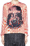 A model is wearing a white and red geometric patterned blouse with Darth Vader printed in black on it. The white and red pattern peeps through the printing. It’s paired with a black and gray geometric printed skirt.