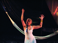 A woman on stage in a light blue dress holding her arms above her head.