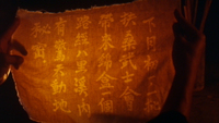 An individual holds up a piece of cloth to candlelight with translucent callligraphy printed on it.