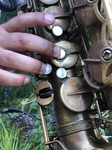 Color image depicting a close-up of fingers pressing down a combination of keys of a tenor saxophone with the right hand.