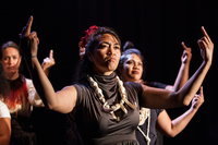 Color production photograph of an ensemble of Samoan women raising both fists high and extending the middle finger.