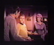 Kirk sits in the captain’s chair, flanked by Nurse Chapel and Mr. Spock