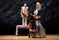 Fig. 4. Black man in white face paint and white suit stands on table; two women downstage in embrace, one a maid in fur, the other a spirit figure in whiteface, a long dress, and tall headdress.