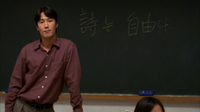 A man stands in front of a chalkboard with yellow calligraphy written on it.