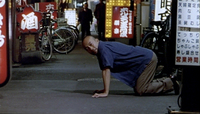 A character is down on all fours on a street lined with signs, whch are all covered with calligraphy.