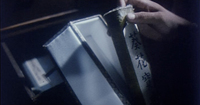 A person takes out a scroll from a box and container. Calligraphy can be seen on the scroll's case.