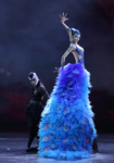 Figure 13.3. A male dancer in black peers around the cascading tail of a giant blue peacock, Yang Liping. Yang lifts her left hand in the peacock head pose and glances at the audience.