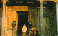 A man walks through an entranceway with a sign above it with engraved calligraphy.