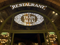 Le Train Bleu restaurant, Paris. The lettering of the sign is white against gold metal. Chandeliers from inside the restaurant diffuse gold light outwards.