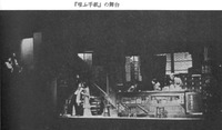 Figure 7.1: A production still of the stage of The Laughing Letter. Four actors in a pharmacy. One of the screens used in the production is visible outside the proscenium arch stage right.