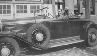 Bradford Ropes sits with a confident smile in a Cadillac convertible, with a shaggy dog behind him, ca. 1930s.