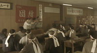 Four men raise their hands towards a classroom with calligraphic writing on the banner and posters behind them