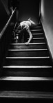 Black-and-white photograph of a female figure in white undergarments crawling down a staircase.