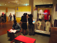 Three people view a screen next to a case of T-shirts.