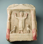 Color photograph of a limestone funerary marker carved with a standing male figure flanked by two small jackals.