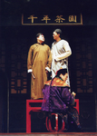Sky High (Zhao Zi-qiang) and Skin Don't Laugh (Chin Shih-chieh), standing on table, performing a crosstalk routine for Lord Beile (Ni Minran), seated with back to the audience, while Hell (Lee Chien-chang), one knee on the floor, waits on Lord Beile.