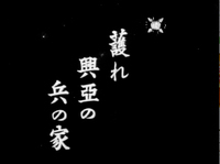 White vertical Japanese pre-titles are superimposed on a black matte background in black-and-white cinematography. This pre-title appears right before the film's production title, before the film begins in earnest. It reads, "Defend the homes of those who fight for a greater Asia."