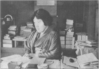 Akiko sits at a desk covered in books and papers.