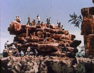 Workers dig and chip away at a large, rocky mountaintop.