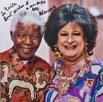 A black man (Nelson Mandela) and a white woman (Pieter-Dirk Uys in drag) smile at the camera. Writing in the upper left corner reads: “To Evita, Best wishes to a wonderful lady—Nelson Mandela.”