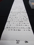 Photograph of black calligraphy on unfurled white paper, on black table.