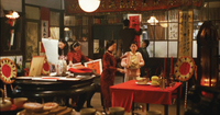 A film still depicting the interior of a busy room, decorated in red and extensively with calligraphy.